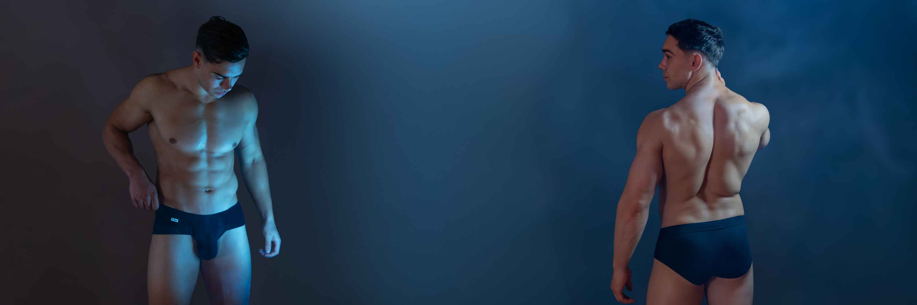 Two men in black trunks standing against a dark blue background