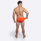 Man wearing bright orange briefs on a white background